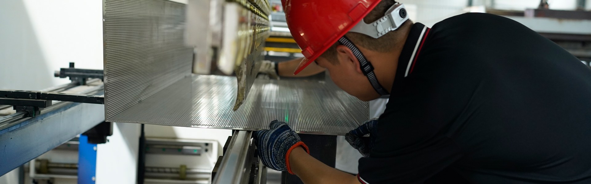 The worker is placing the metal plate on the bending machine.